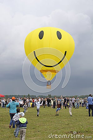 Balloon with the smiley face symbol on it flying above the field with crowd of people walking around Editorial Stock Photo