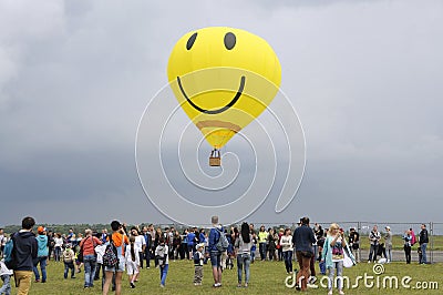 Balloon with the smiley face symbol on it flying above the field with crowd of people walking around Editorial Stock Photo