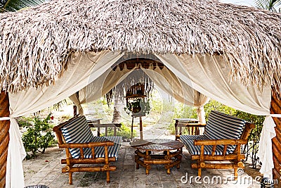 Bamboo benches with cushions, low round table are in an open thatched pavilion Stock Photo