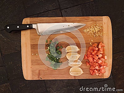Bamboo cutting board with chef knife and prepared chives lemon zest and tomatoes Stock Photo