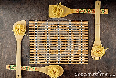 Bamboo spatulas with fettuccine paste around a bamboo napkin on a wooden background Stock Photo