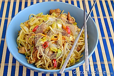 Bami goreng, fried noodles with cabbidge, soja sauce, chili pepper, pork in a blue ceramic bowl on a striped wooden Stock Photo