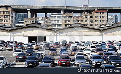 Many cars are parked at the outdoor parking lot with garage building and taller building, Expressway and blue sky. Editorial Stock Photo