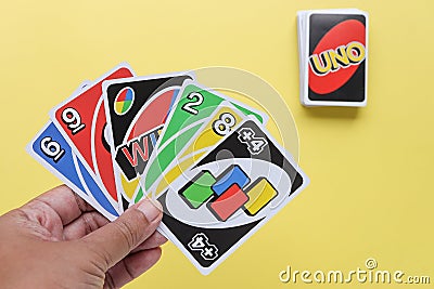 Bangkok, Thailand : August 13, 2023 : Uno game cards in the player's hand on light yellow background. Editorial Stock Photo