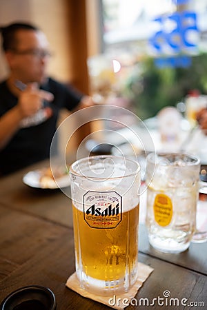 Cold Asahi beer mug on a dark brown wooden table in a Japanese izakaya restaurant Editorial Stock Photo