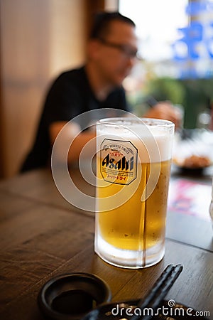 Cold Asahi beer mug on a dark brown wooden table in a Japanese izakaya restaurant Editorial Stock Photo