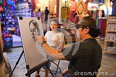 BANGKOK, THAILAND - November 14, 2016: Unidentified artist drawing pencil portrait of the tourist at ASIATIQUE The Riverfront Editorial Stock Photo