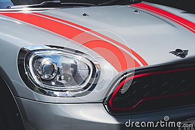 Close up of headlight with red stripes on bonnet surface of Bronze MINI COOPER S COUNTRYMAN car in outdoor parking area Editorial Stock Photo