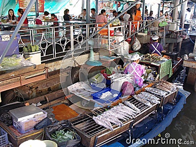 People eating at tables the fish that a woman cooks in her boat at the Taling Chan Floating Market in Bangkok Editorial Stock Photo