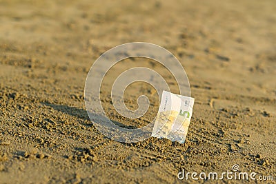 Banknote of value of five euro in the the sand on the beach. Concept of cheap travel and vacation. Stock Photo