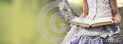 Banner Asian Girl holding book reading at green park in nature garden. Panorama Young todler girl relaxation read book. Happy Stock Photo