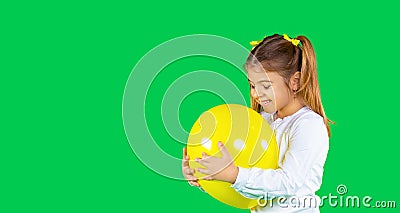 Banner. Cute preschool blonde girl with two pigtails hugs a illuminating color balloon. Green background and side space Stock Photo