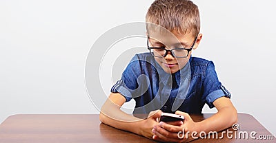 Banner Portrait of smiling boy with glasses using mobile phone on school Desk on white background Modern mobile and communications Stock Photo