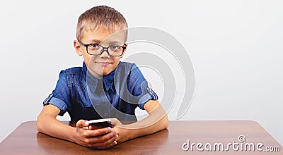 Banner Portrait of smiling boy with glasses using mobile phone on school Desk on white background Modern mobile and communications Stock Photo