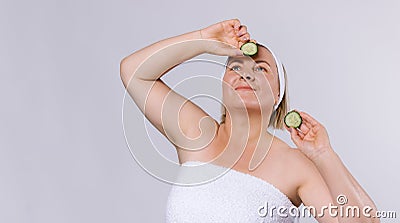 Banner. Senior woman with well-groomed skin and a bandage on her head looks upwards holding cucumber slices in her hands Stock Photo