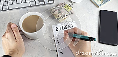 banner with Top view of female hands writing in notepad, note with words BUDGET, cup of coffee and money on table Stock Photo