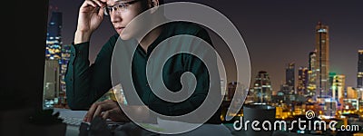 Banner of young asian man sitting on desk table work late and hard with computer laptop at office with night light city view Stock Photo