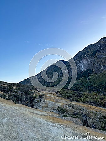 a stretch of rocks covered with small trees with a backdrop of green mountains and blue skies Stock Photo