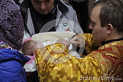 Baptizing for baby. Man and woman standing with a baby on hands and priest cutting off a patch of hairs from head of child Editorial Stock Photo