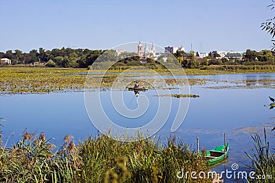 Bar, Ukraine: unknown fisherman fishing in a wooden punt on river Riv, St. Anna Roman Catholic Church Editorial Stock Photo