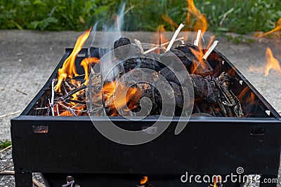 Barbecue grill with burning charcoal and wood - black rectangular grill - orange and yellow flames - blurred concrete background Stock Photo