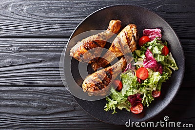 Barbecue serving of grilled chicken drumsticks and fresh vegetable salad closeup. Horizontal top view Stock Photo