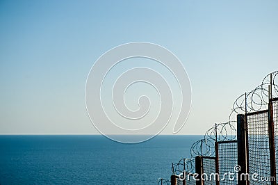 Barbed razor fencing on state border against illegal immigration near sea sky Stock Photo