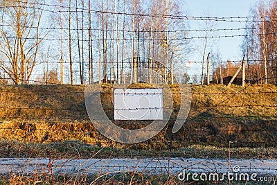 Barbed wire fence protects the danger zone. White sign board Stock Photo