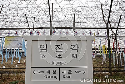 Barbed wire fence separates South from North Korea - South Korean flags attached to fence - Asia - SIGN POINTS TO GAESEONG AND SEO Editorial Stock Photo