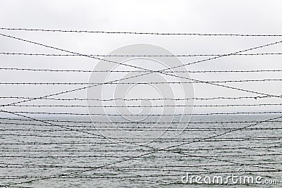 Barbed wire on high steel fence on blue sky and sea background Stock Photo