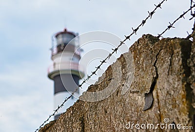 barbed wire and stone fence, behind them a lighthouse. concept of slavery, dictatorship and totalitarianism Stock Photo