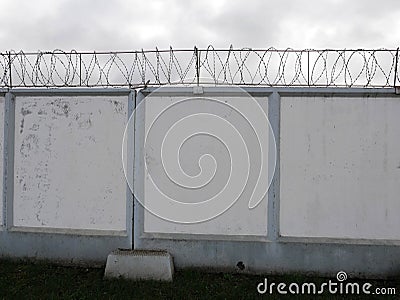 Barbed wire on white fence. Concrete wall, on the background barbed wire, prison concept, space for text Stock Photo