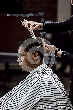 The barber is cutting a man`s hair holding scissors and comb in his hands opposite the mirror in a barbershop Stock Photo