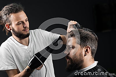 Barber dries the hair of a handsome bearded man after a fashionable haircut. The work of a hairdresser during the Stock Photo