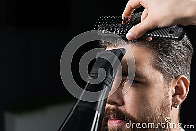 Barber dries the hair of a handsome bearded man after a fashionable haircut. The work of a hairdresser during the Stock Photo