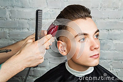 Barber hair styling of young guy in the barbershop on brick wall background, hairdresser makes hairstyle for a young man. Stock Photo