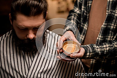 barber holds round jar of hair styling gel near the head of male client. Stock Photo