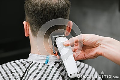 Barber`s hand with a clipper cuts the back of a man`s neck. Haircuts in barbershop. Hairdresser shaves a young man hair clipper. Stock Photo