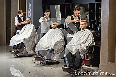 Barbers grooming and styling haircuts of clients in barbershop. Stock Photo