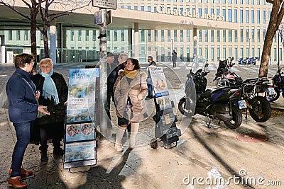 Barcelona - December 15, 2023: Group of people chatting on an urban street next to a religious advertisement. Editorial Stock Photo