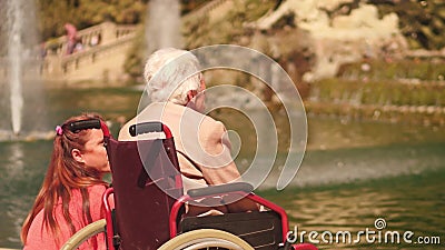 BARCELONA, SPAIN - APRIL, 16, 2017. Handicapped senior woman in a wheelchair and her daughter near park fountain Editorial Stock Photo