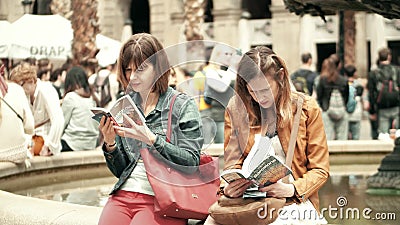 BARCELONA, SPAIN - APRIL, 16, 2017. Two young women reading city tourist guide books near the fountain Editorial Stock Photo