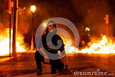 Barcelona, Spain - 18 october 2019: catalan protest with joker mask stand in front of fire during riots with mossos police at Editorial Stock Photo