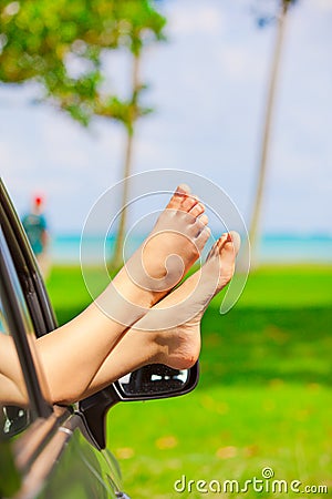 Bare feet of female sticking out car window, by ocean Stock Photo