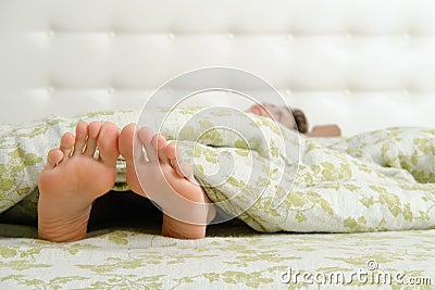 Bare female feet sticking out from under the blanket Stock Photo