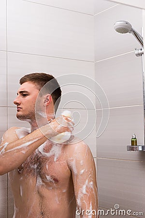 Bare young male rubbing himself a foam sponge bath in shower cab Stock Photo