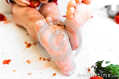 A barefoot baby plays at biting red tomatoes and smearing its juice Stock Photo
