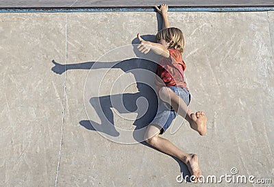 barefoot child makes a funny shadow on the asphalt, lying on the ground and showing a thumbs up Stock Photo