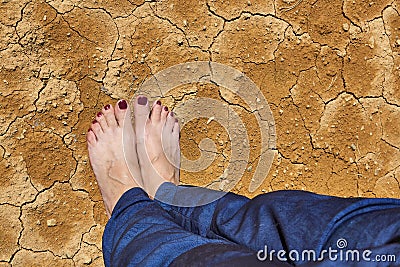 Barefoot female feet in jeans stand on dry cracked ground Stock Photo