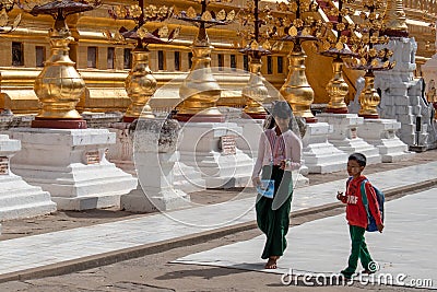 Barefoot kids boy and girl back from school walking clockwise at Shwezigon pagoda with thanaka on their faces. Wearing traditional Editorial Stock Photo